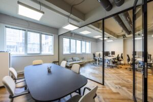 Moderne kantoorruimte aan de De Ruijterkade met vergadertafel, glazen scheidingswand en werkplekken met computers.